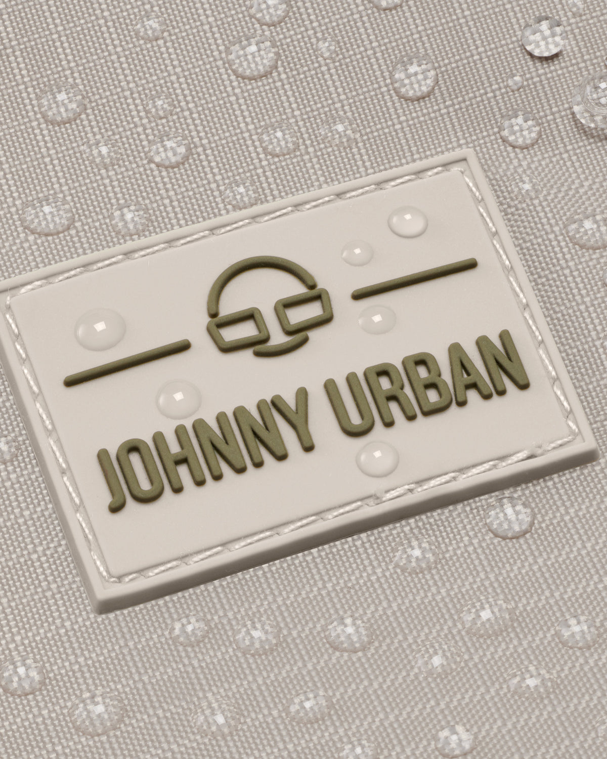 Detailansicht des Johnny Urban Logos auf einem wasserabweisenden, beigefarbenen Rucksack Harper mit Wassertropfen
