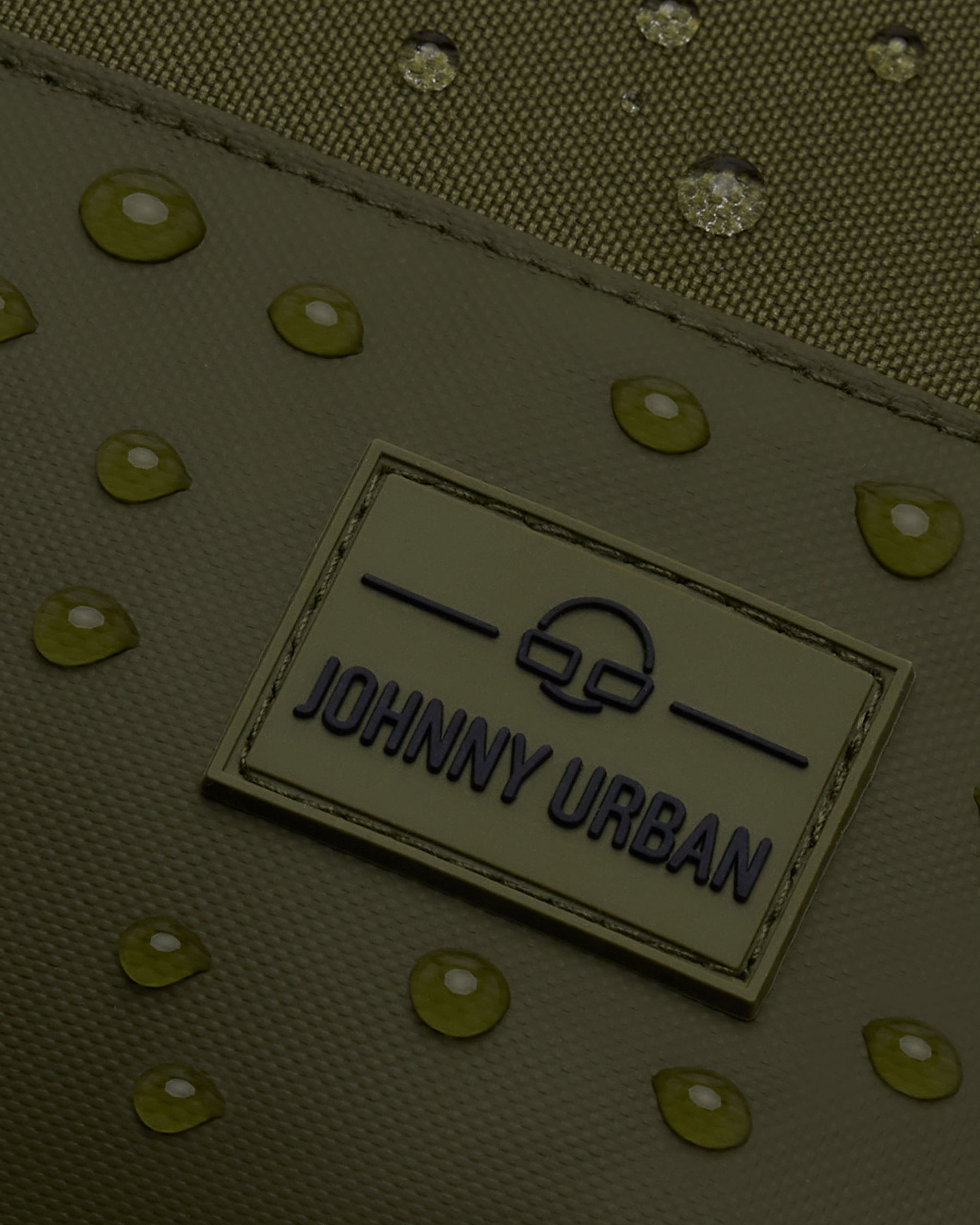 Nahaufnahme des wasserabweisenden, olivfarbenen Rucksacks 'Mika' von Johnny Urban mit Markenlogo und Wassertropfen