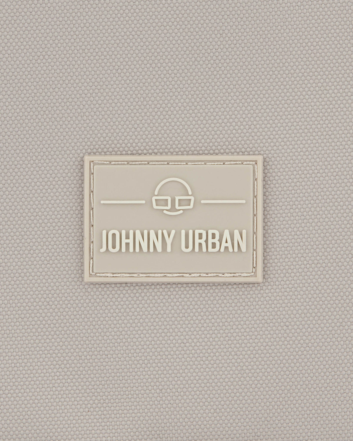 Beiges Textillogo mit dem Schriftzug 'Johnny Urban' und einem stilisierten Brillensymbol