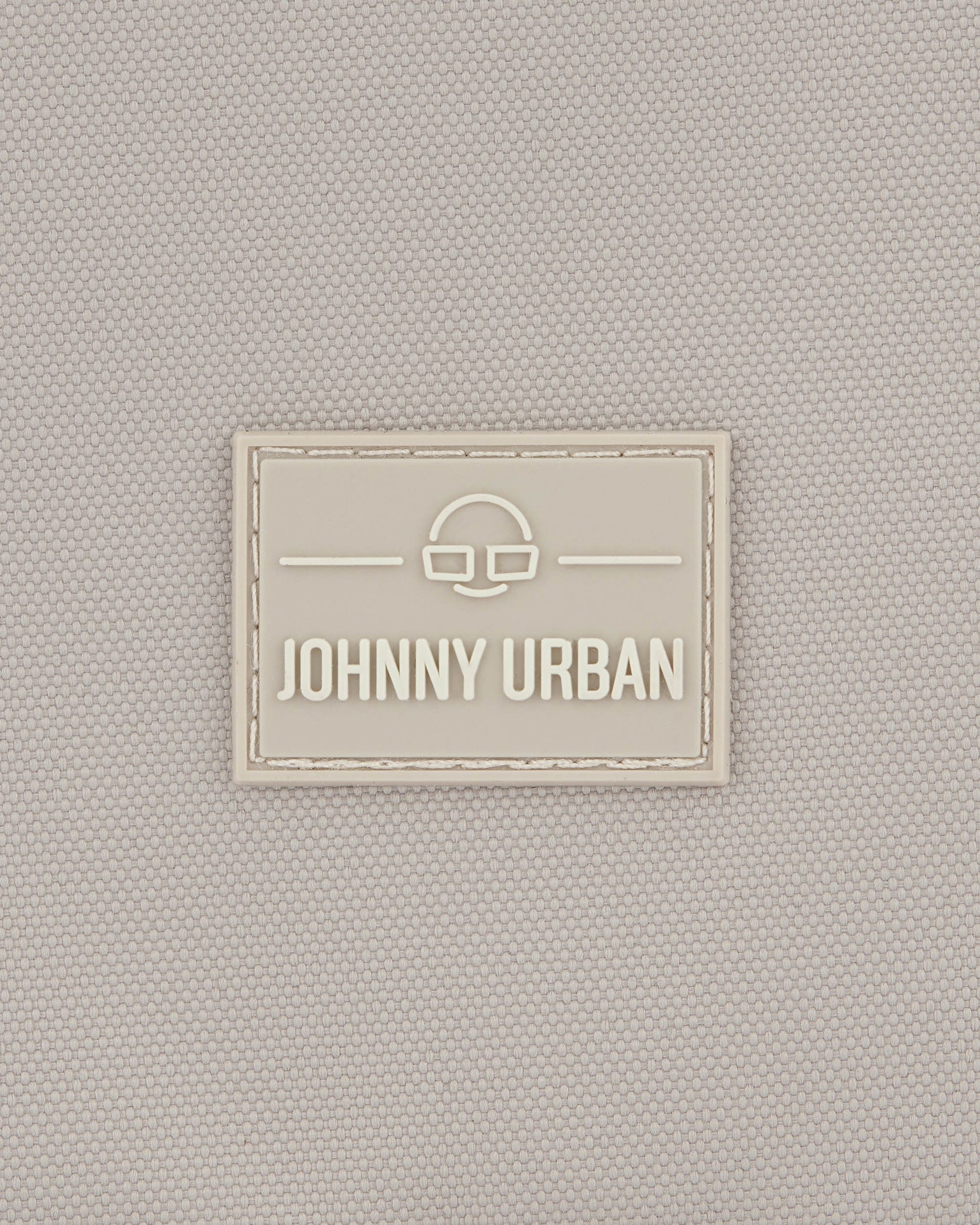 Beiges Textillogo mit dem Schriftzug 'Johnny Urban' und einem stilisierten Brillensymbol