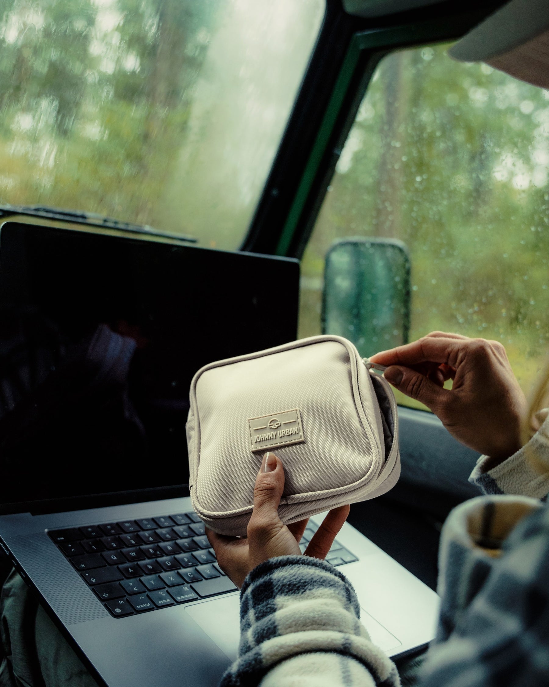 Beige Tech Organizer 'Ted' von Johnny Urban in Händen vor einem Laptop im Auto bei Regen