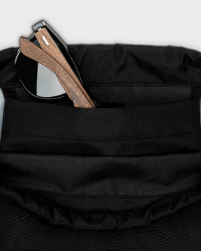 Schwarzer Turnbeutel 'Blake' mit verstecktem Fassungsfach, aus dem Sonnenbrille mit Holzbügeln hervorschaut
