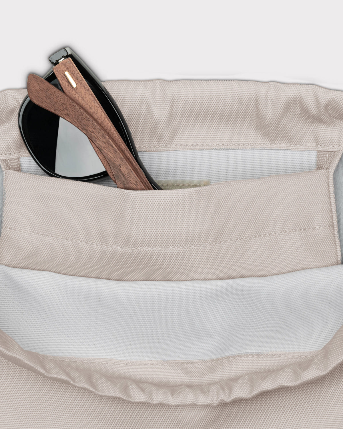 Beige Turnbeutel 'Blake' mit Innenfach, darin eine schwarze Sonnenbrille mit Holzgestell
