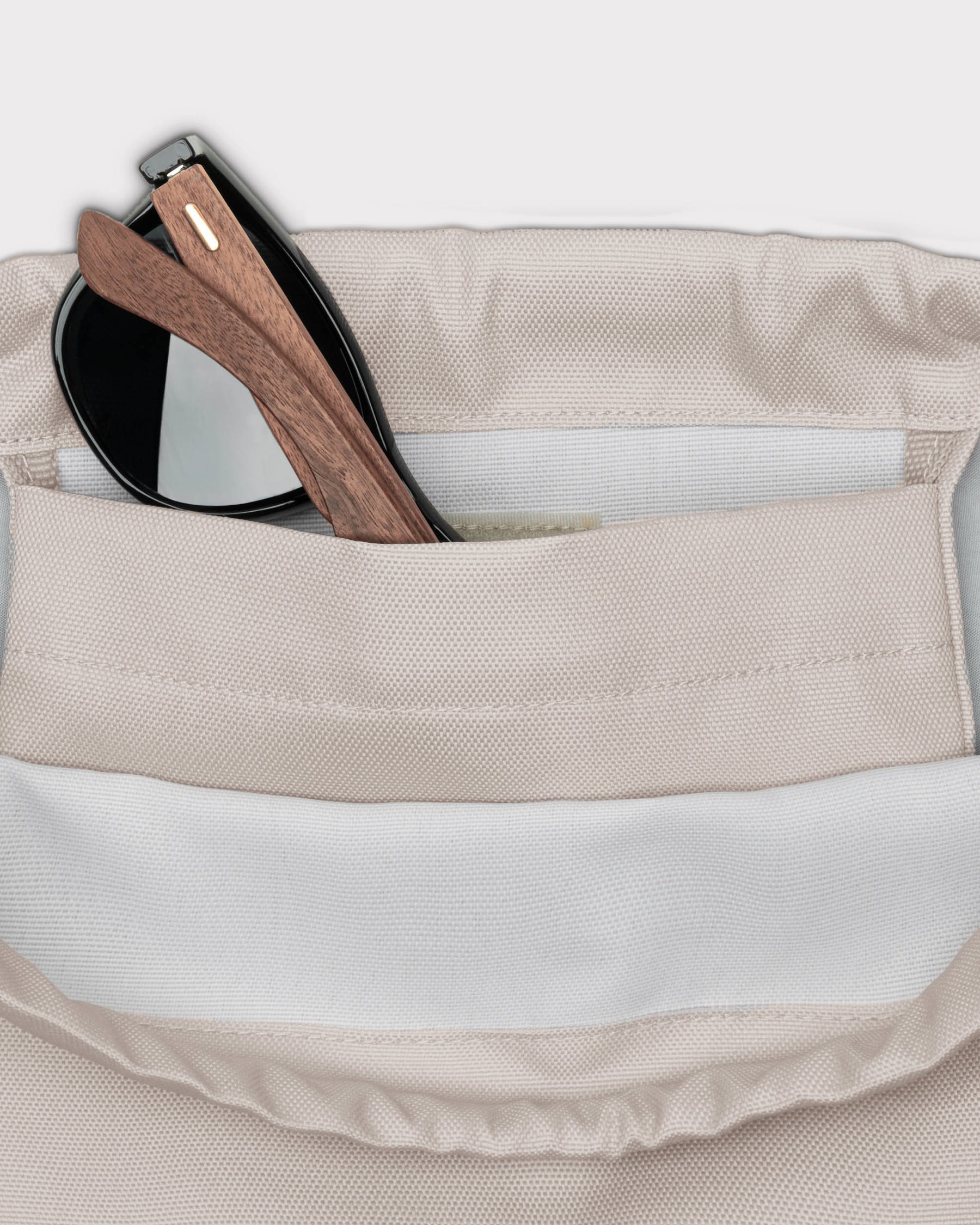 Beige Turnbeutel 'Blake' mit Innenfach, darin eine schwarze Sonnenbrille mit Holzgestell