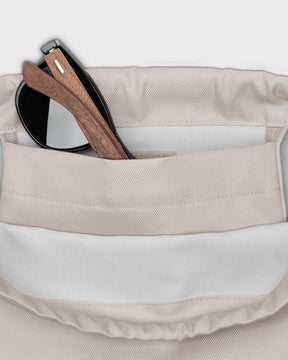 Beige Turnbeutel 'Blake' mit Innenfach, darin eine schwarze Sonnenbrille mit Holzgestell