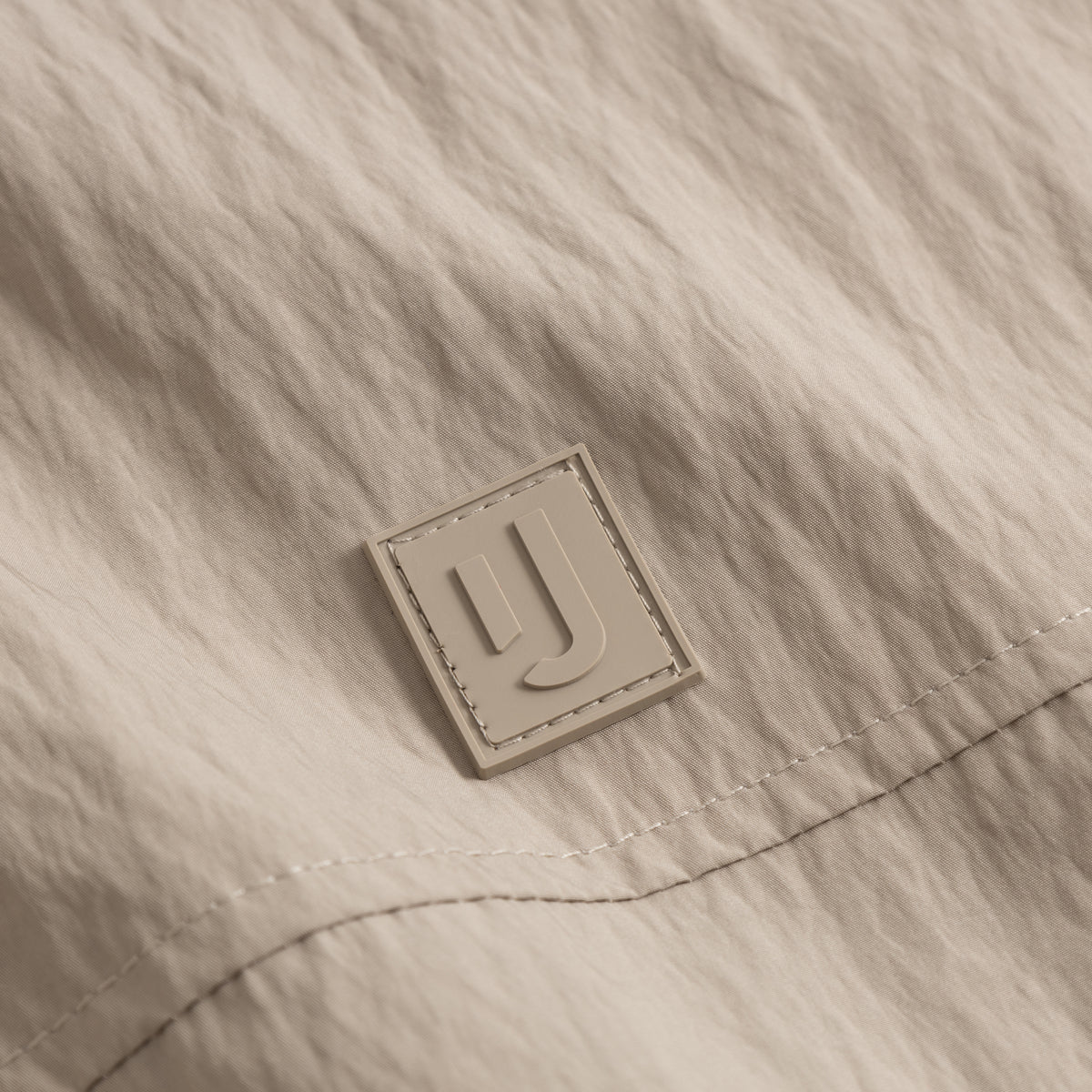 Nahe Aufnahme des Logos auf der beigen Übergangsjacke 'Lennon' von Johnny Urban