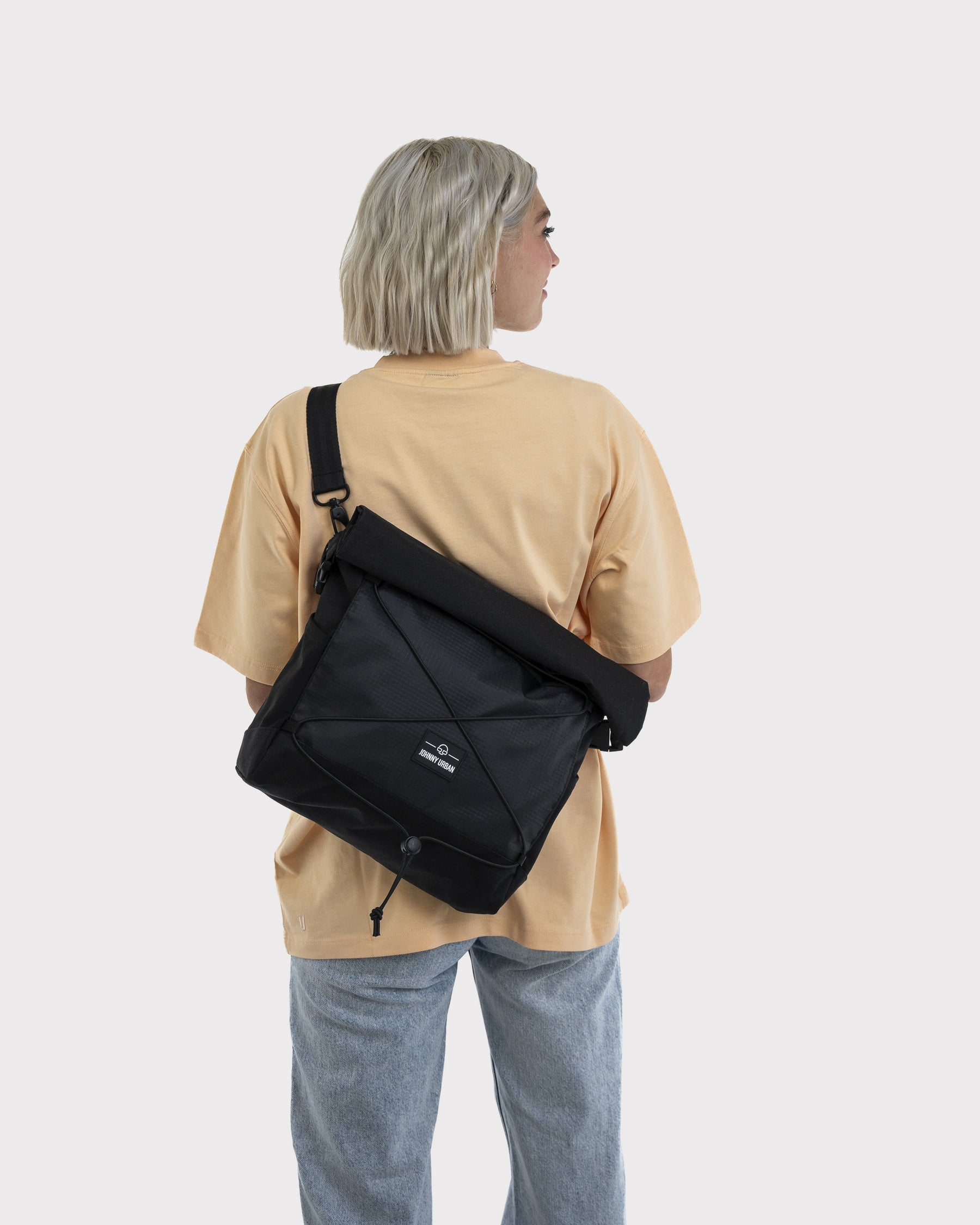 Frau mit schwarzer Umhängetasche 'Dylan' von Johnny Urban, trägt beige Shirt und blaue Jeans, Rückansicht