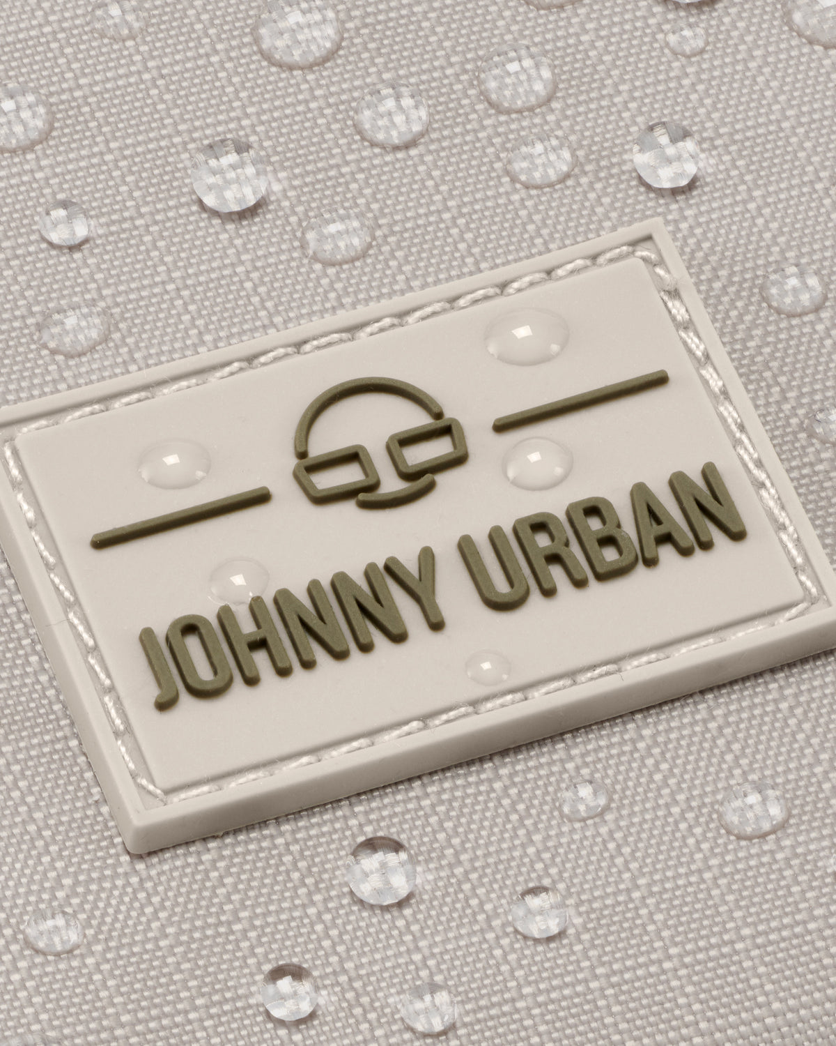 Nahaufnahme des wasserabweisenden beigefarbenen Stoffs mit 'Johnny Urban' Logo auf Umhängetasche Jayden