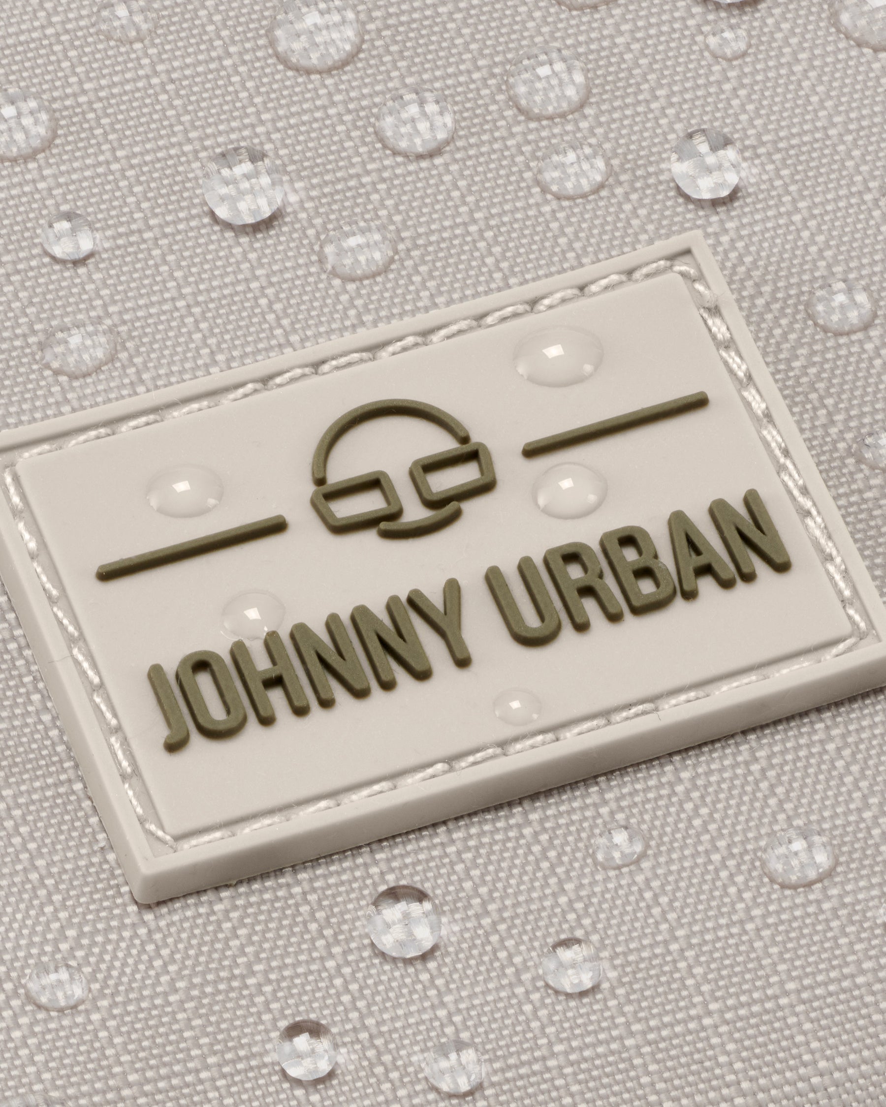 Nahaufnahme des wasserabweisenden beigefarbenen Stoffs mit 'Johnny Urban' Logo auf Umhängetasche Jayden