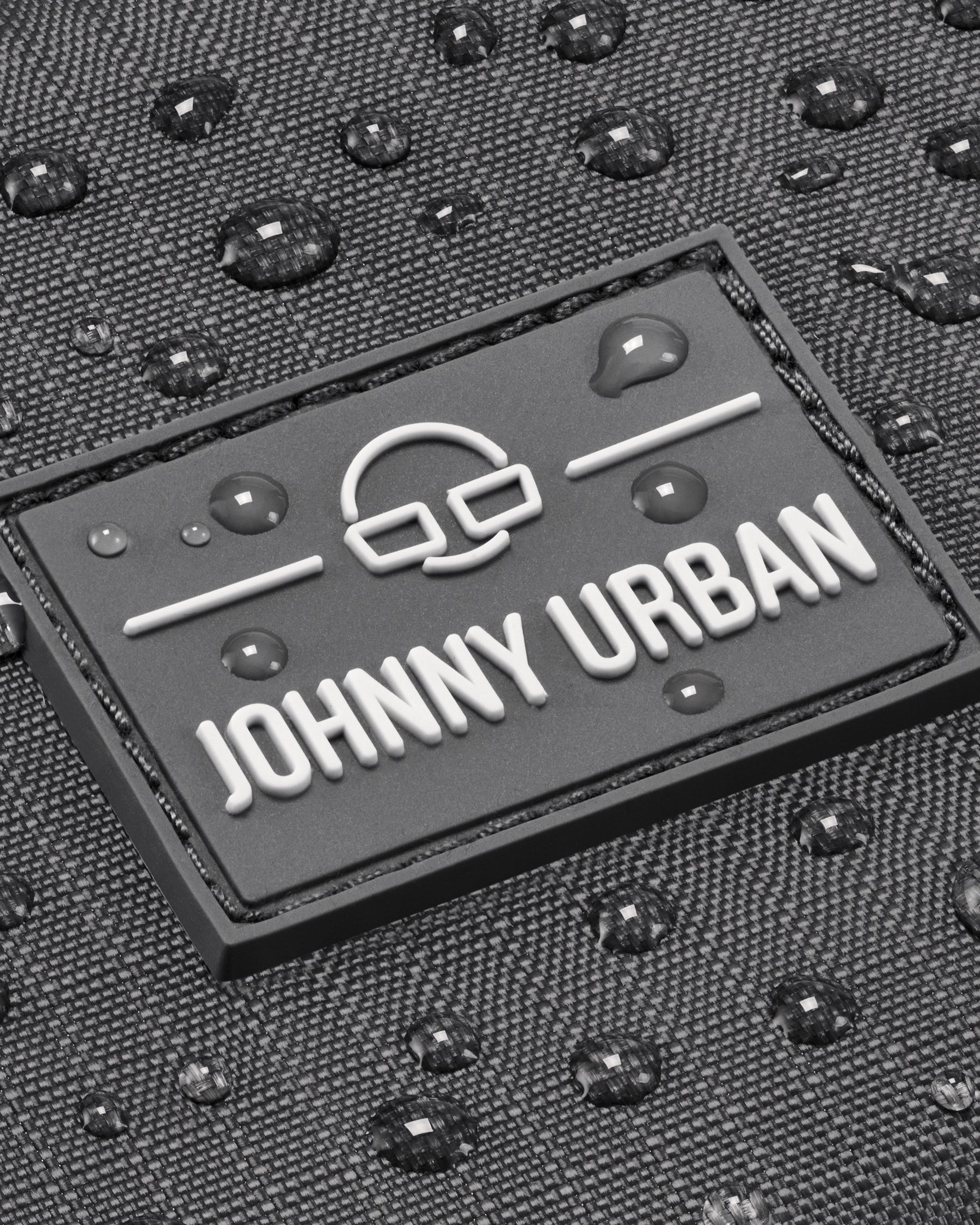 Nahaufnahme des Johnny Urban Logos auf grauem, wasserabweisendem Stoff mit Wassertropfen