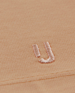 Nahaufnahme der rosa Stickerei des Buchstabens ‚JU‘ auf einem pfirsichfarbenen T-Shirt ‚Sammy‘ von Johnny Urban
