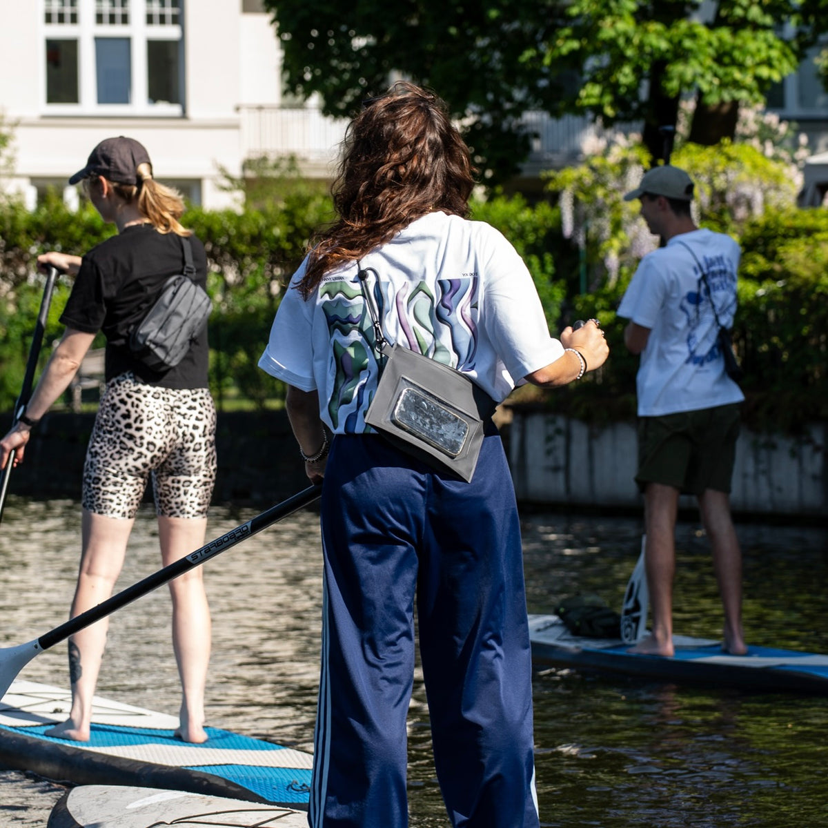 Drei Personen beim Stand-up-Paddling, eine trägt die schwarze Dry Bag 'Alfie' von Johnny Urban um die Hüfte