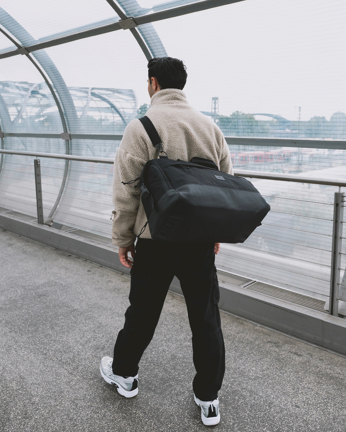 Mann läuft am Flughafen und trägt die  Reisetasche Milan in schwarz crossbody 