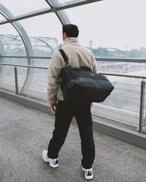 Mann läuft am Flughafen und trägt die  Reisetasche Milan in schwarz crossbody 