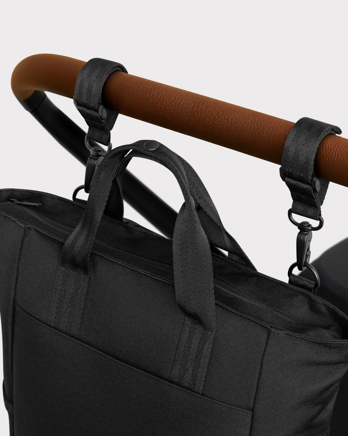 Schwarze Wickeltasche 'Blair' aus robustem Material, an braunem Kinderwagen mit zwei schwarzen Gurten befestigt