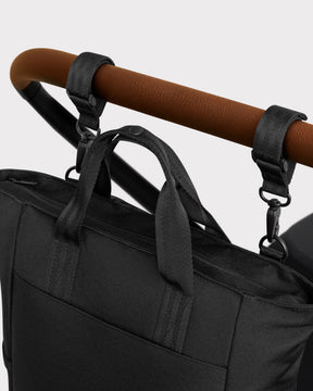 Schwarze Wickeltasche 'Blair' aus robustem Material, an braunem Kinderwagen mit zwei schwarzen Gurten befestigt