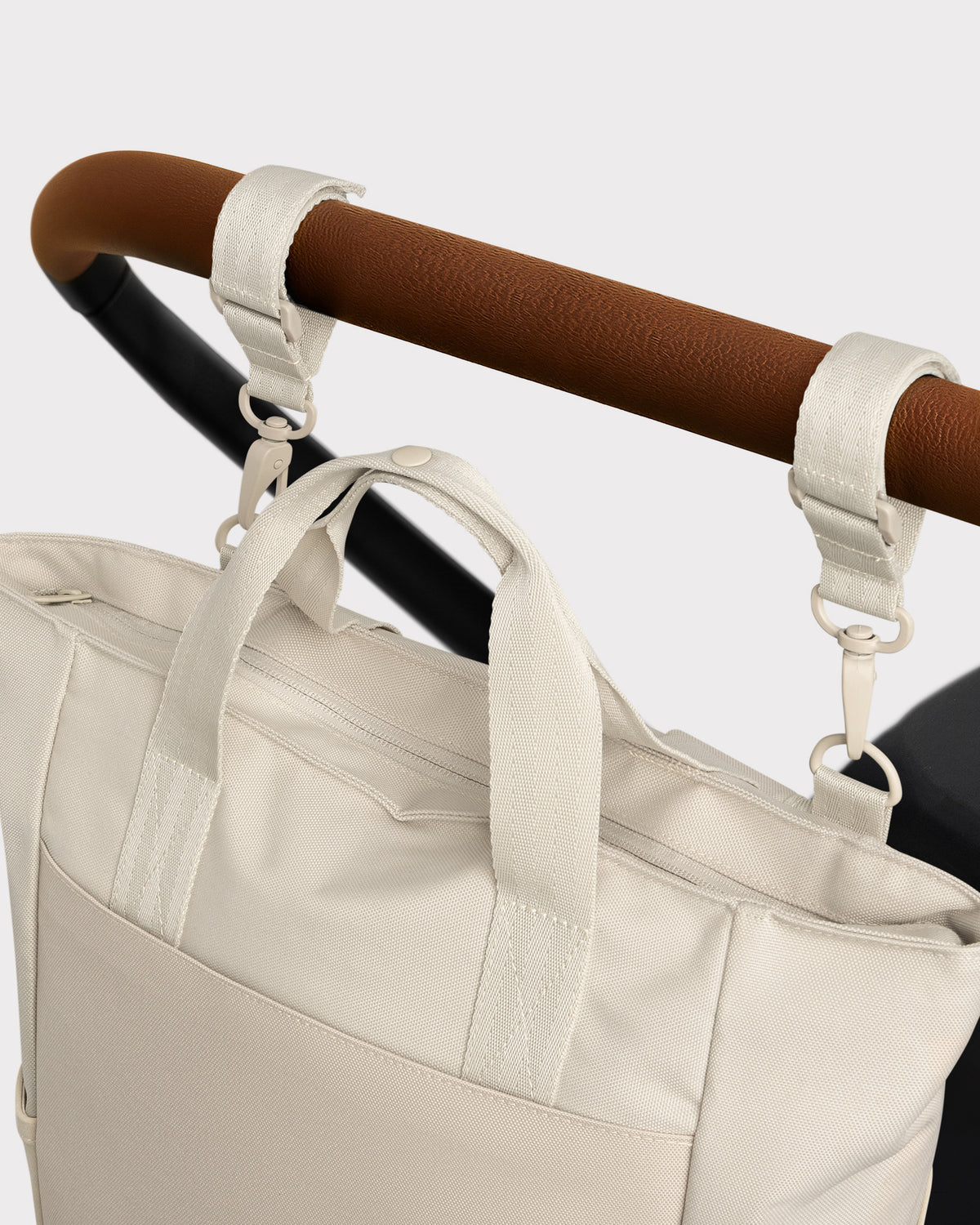 Wickeltasche 'Blair' in Beige, befestigt am braunen Griff eines Kinderwagens mit zwei Haken