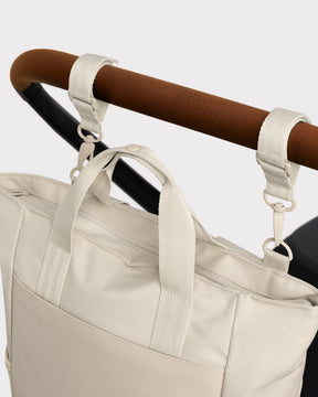 Wickeltasche 'Blair' in Beige, befestigt am braunen Griff eines Kinderwagens mit zwei Haken