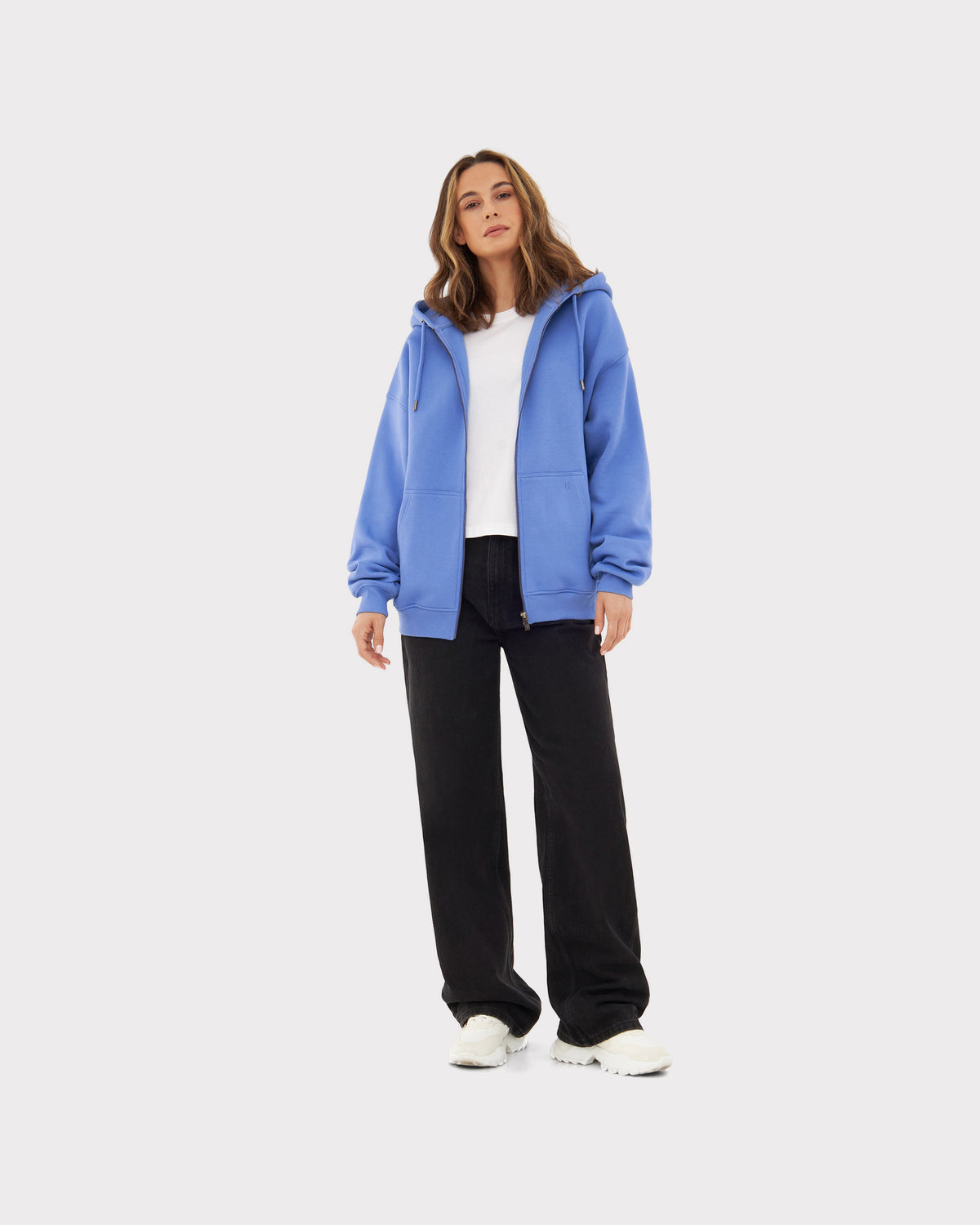 Frau trägt oversized Zip-Hoodie 'Caleb' in blau-lila, weiße T-Shirt, schwarze Hose und weiße Schuhe