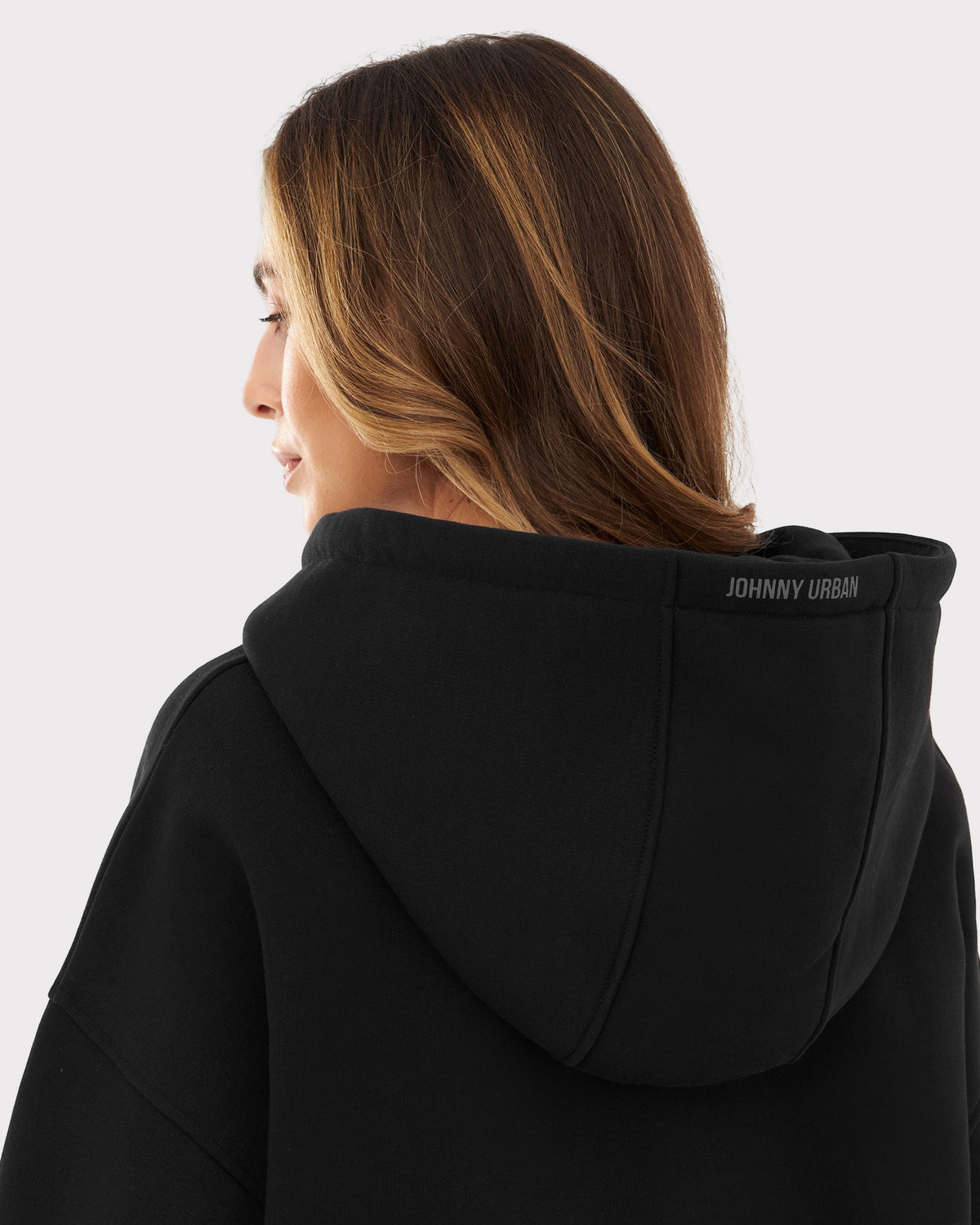 Rückansicht einer Frau mit schwarzen oversized Zip Hoodie "Caleb" und Kapuze mit 'Johnny Urban'-Schriftzug