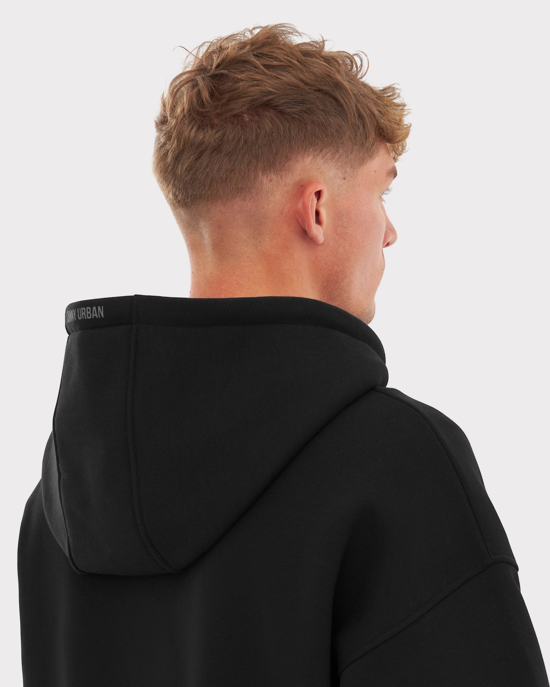 Männliches Modell von hinten trägt schwarzen Oversized Zip Hoodie ‚Caleb‘ mit kapuze und Johnny Urban Schriftzug