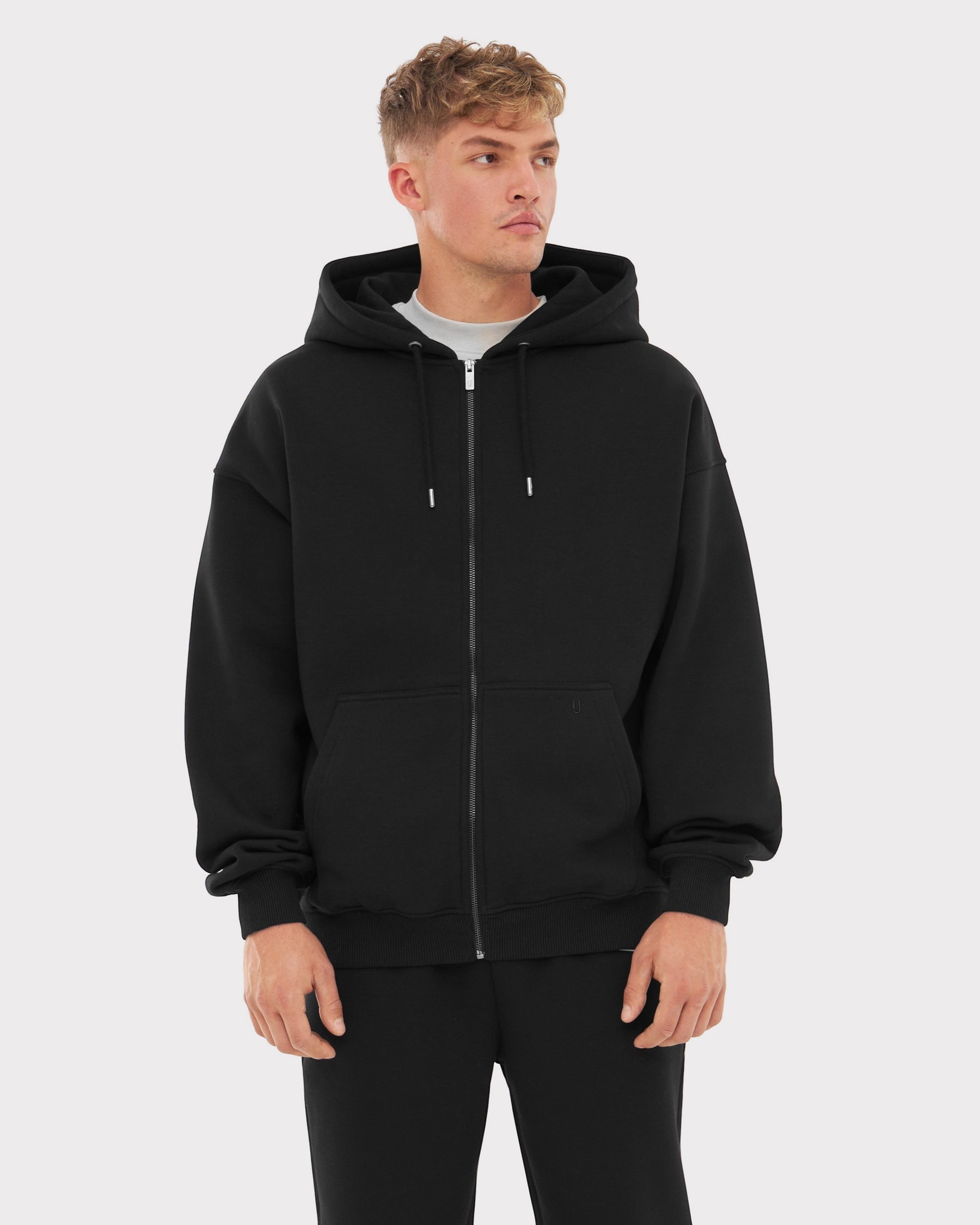 Mann trägt Oversized Zip Hoodie "Caleb" in Schwarz mit Kapuze und Kängurutaschen