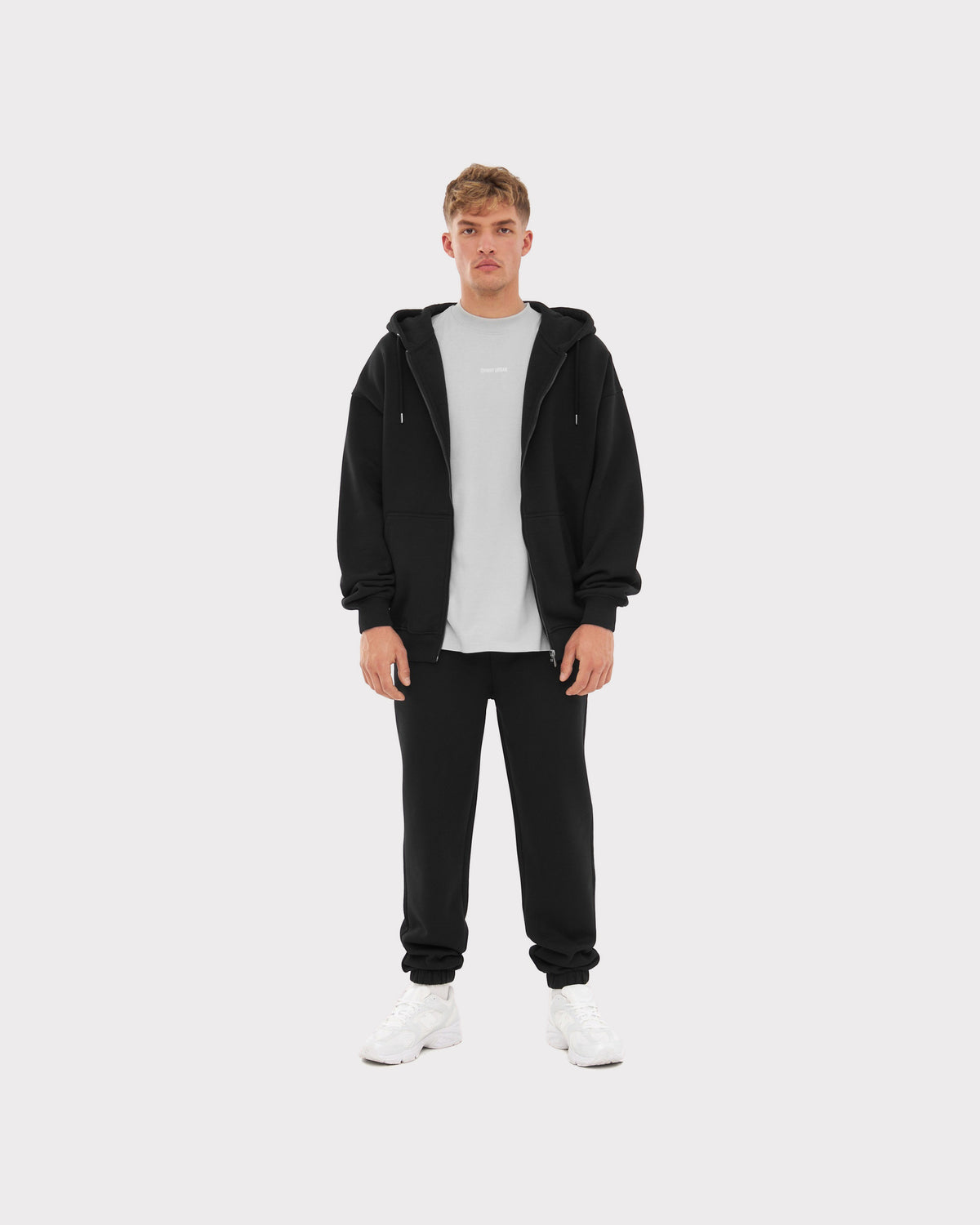 Mann trägt oversized Zip Hoodie 'Caleb' von Johnny Urban in schwarz, dazu schwarze Jogginghose und weißes T-Shirt