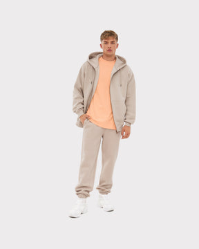 Mann trägt übergroße beige Zip-Hoodie 'Caleb' mit Kapuze, passende Jogginghose und weißer Sneaker