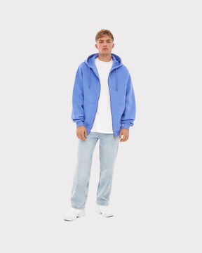Mann trägt oversized Zip-Hoodie 'Caleb' in Blau-Lila, weißes T-Shirt, helle Jeans und weiße Schuhe