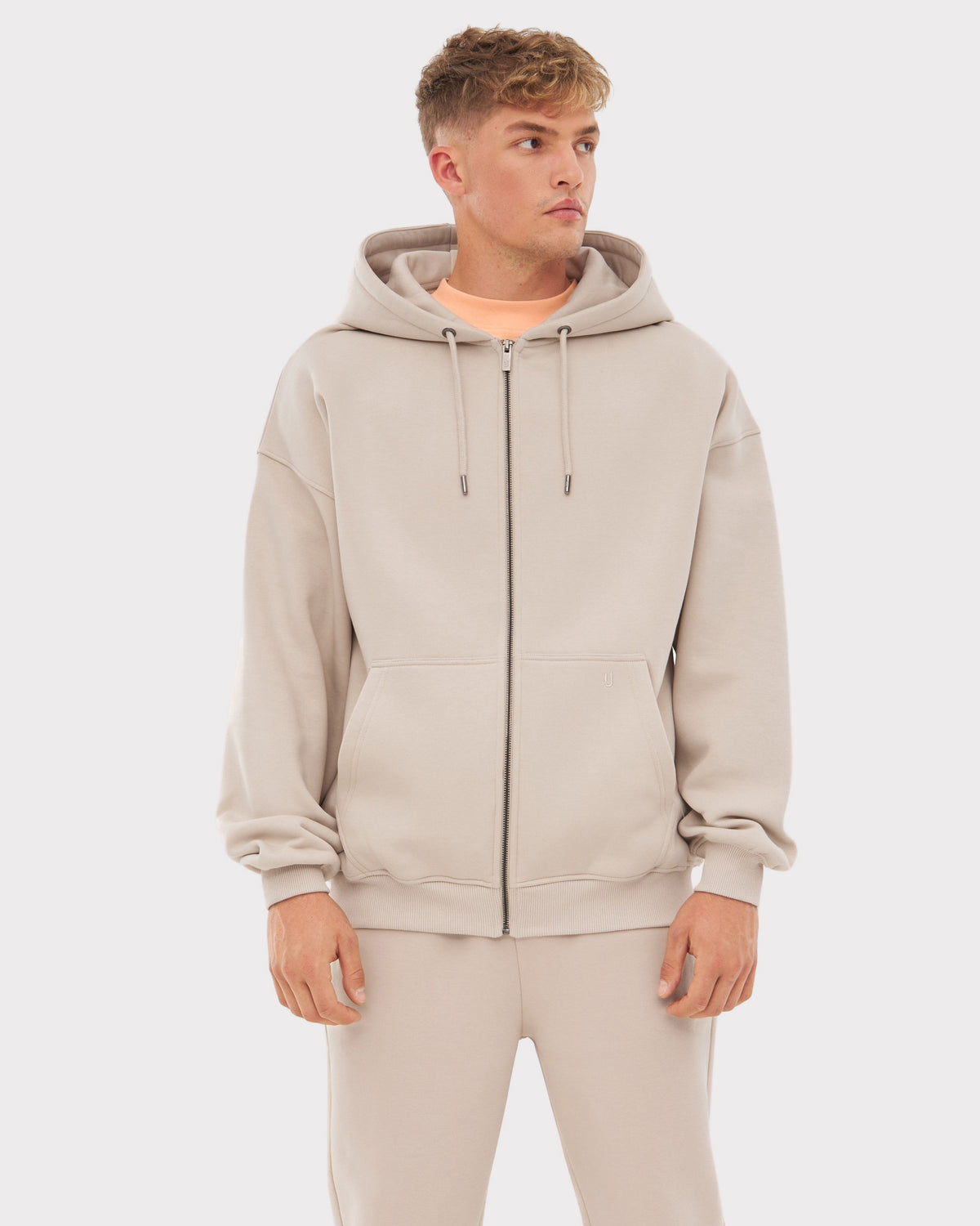 Mann trägt oversized Kapuzenjacke 'Caleb' in Beige mit Reißverschluss und eingearbeiteten Taschen