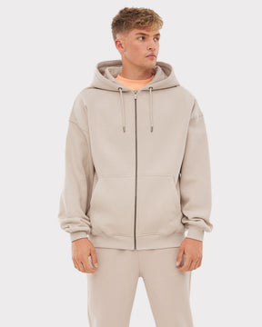 Mann trägt oversized Kapuzenjacke 'Caleb' in Beige mit Reißverschluss und eingearbeiteten Taschen