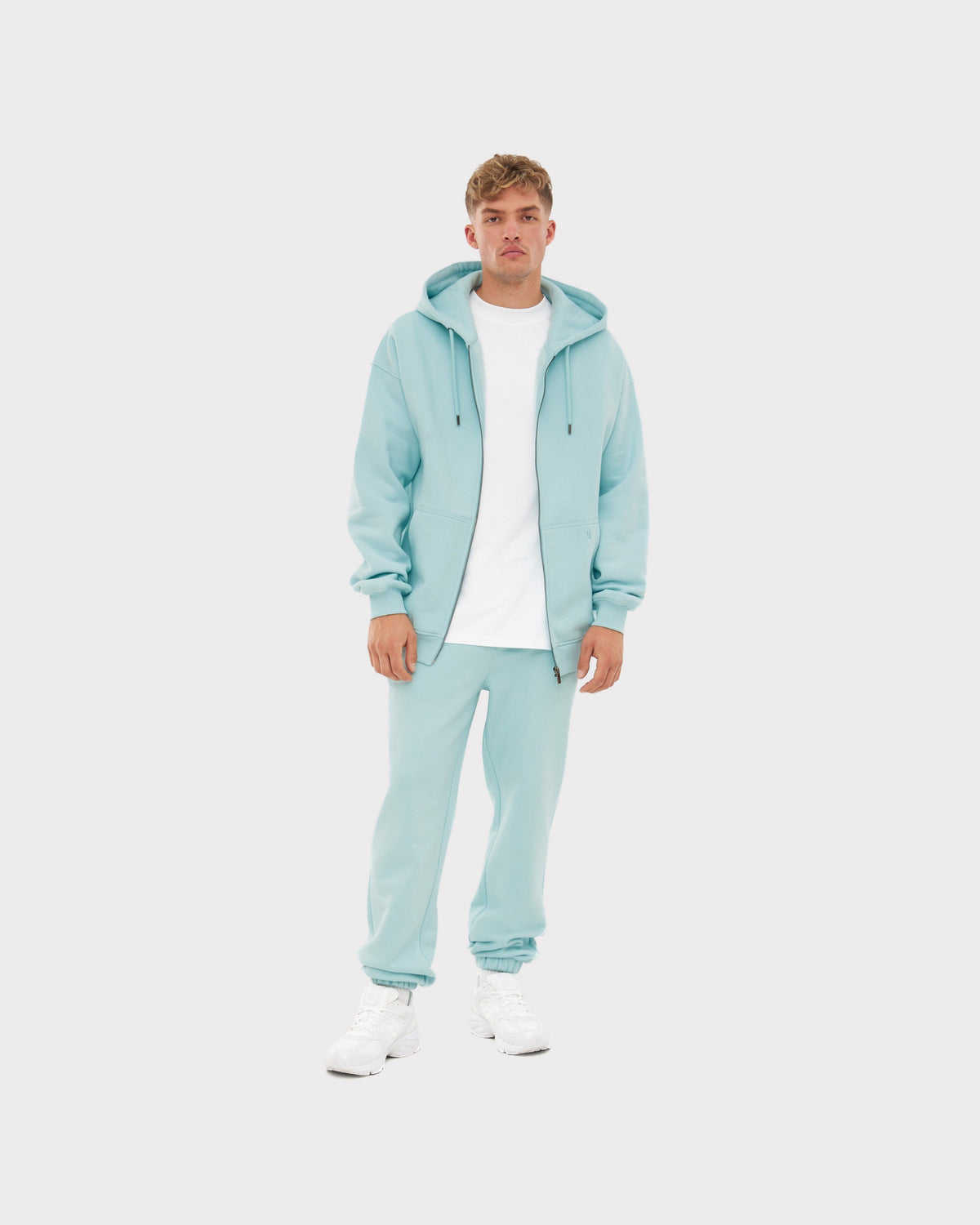 Mann trägt oversized Zip-Hoodie 'Caleb' in eisblau mit passender Hose und weißem T-Shirt