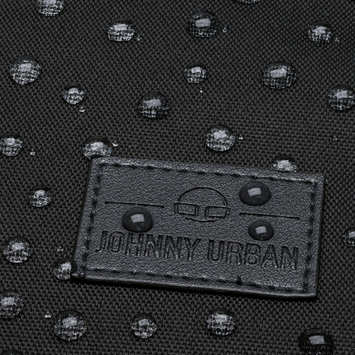 Nahaufnahme von wasserabweisendem schwarzem Textil mit Johnny Urban Lederlabel und Wassertropfen darauf