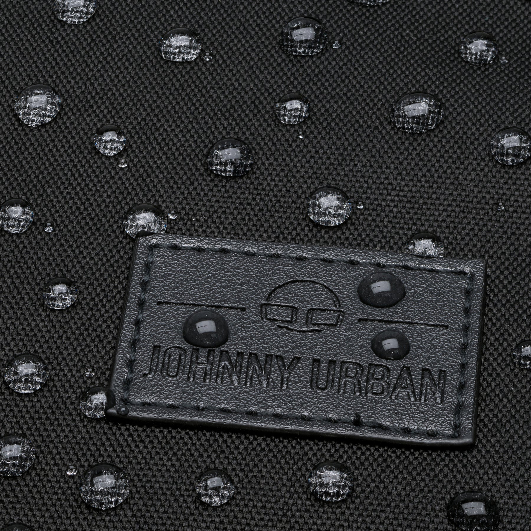 Nahaufnahme von wasserabweisendem schwarzem Textil mit Johnny Urban Lederlabel und Wassertropfen darauf