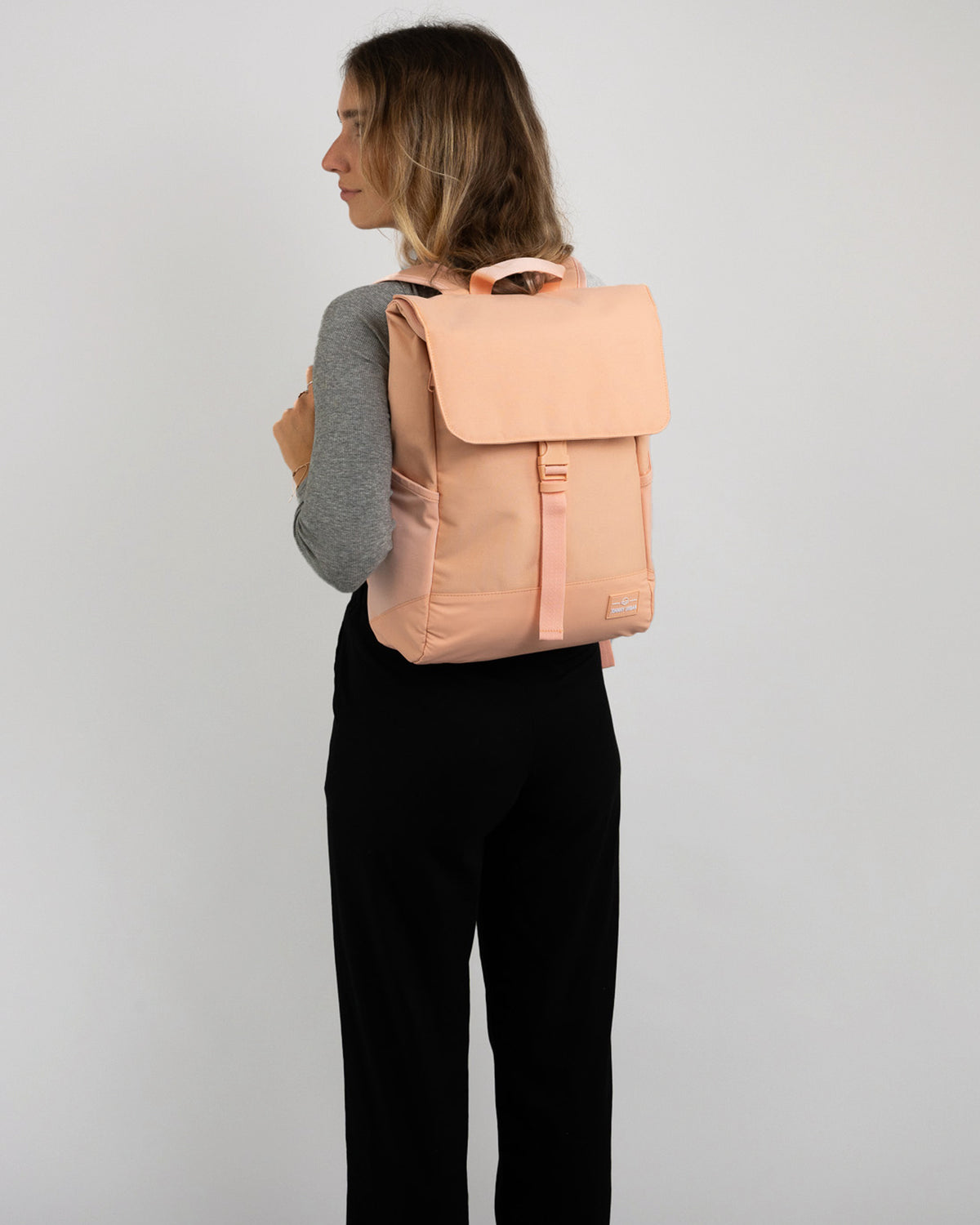 Frau von hinten mit peachfarbenem Rucksack 'Mika', graues Oberteil, schwarze Hose