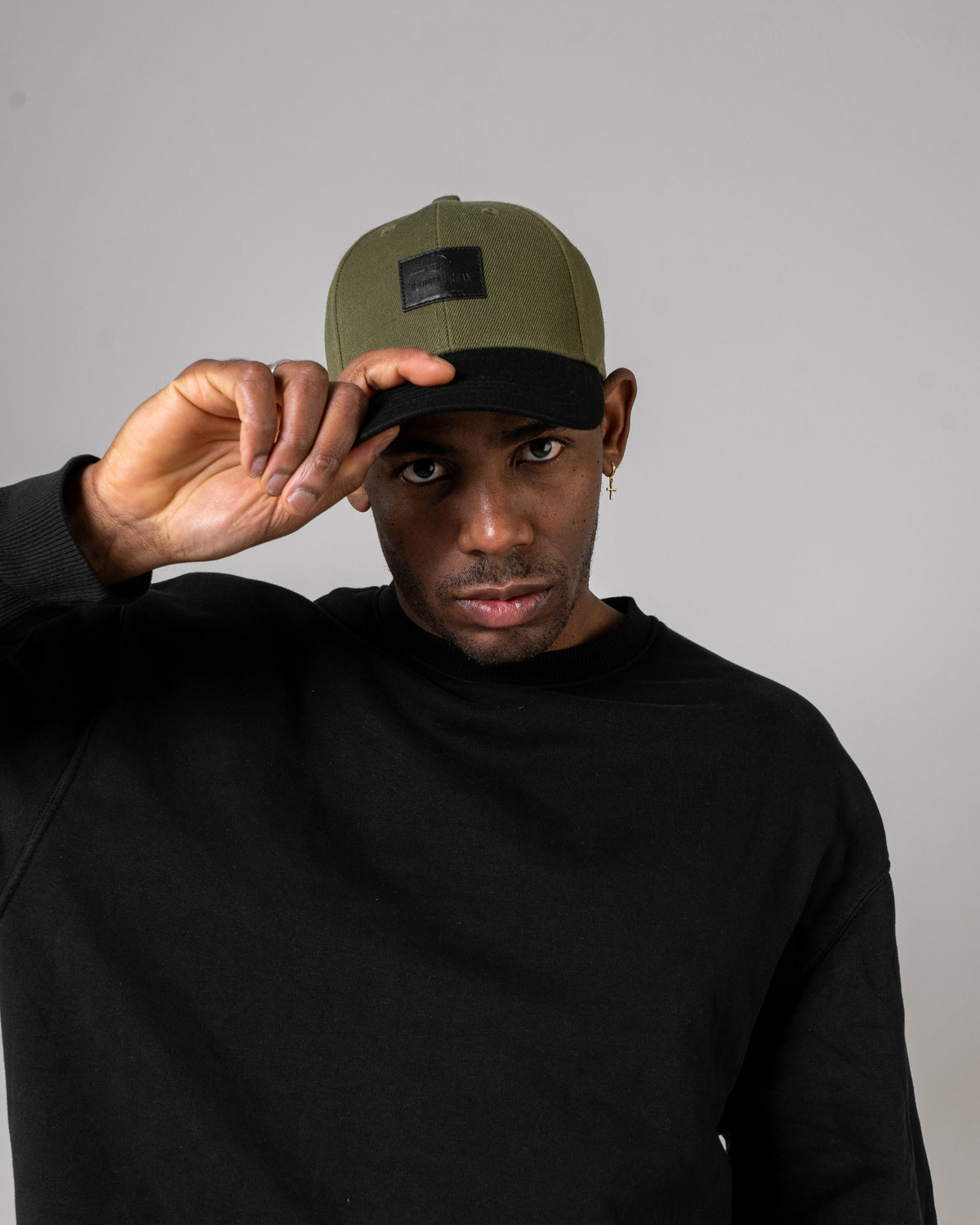 Mann trägt grün-schwarze Johnny Urban Cap 'Dean' und schwarzen Pullover, hebt die Kappe mit der Hand