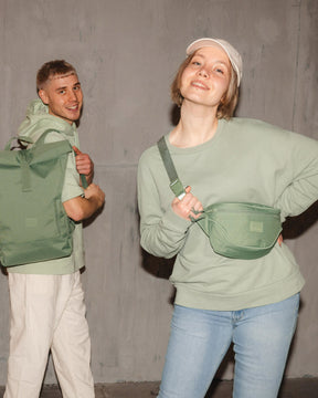 Frau mit grüner Bauchtasche 'Ben' von Johnny Urban, Mann mit grünem Rucksack, beide vor grauer Wand