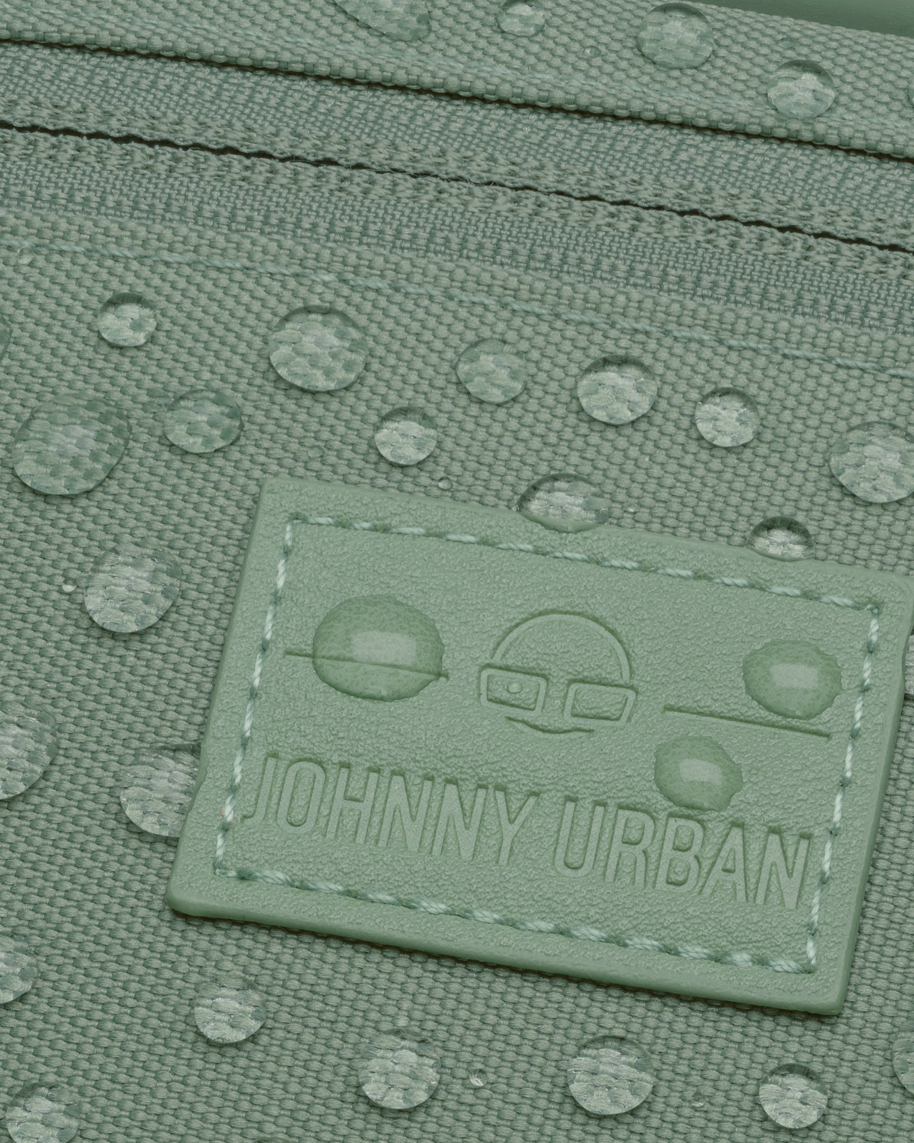 Nahaufnahme der wasserabweisenden grünen Bauchtasche 'Ben' von Johnny Urban mit Tropfen auf der Oberfläche