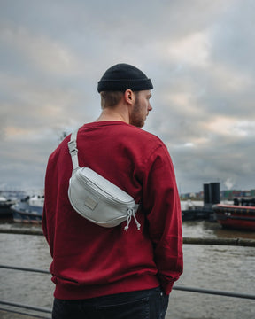 Mann trägt graue Bauchtasche 'Ben' von Johnny Urban über rotem Pullover am Hafen