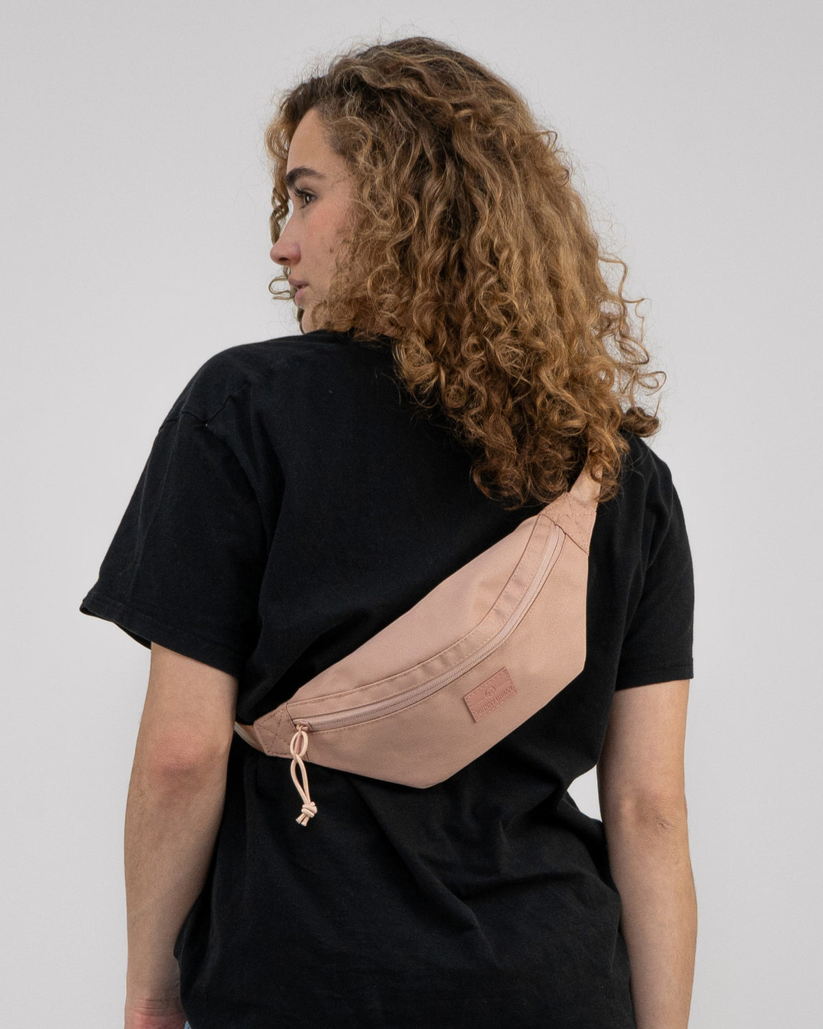 Frau mit lockigen Haaren trägt rosa Bauchtasche 'Erik Small' von Johnny Urban quer am Rücken