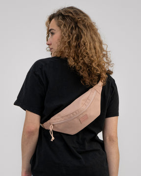 Frau mit lockigen Haaren trägt rosa Bauchtasche 'Erik Small' von Johnny Urban quer am Rücken
