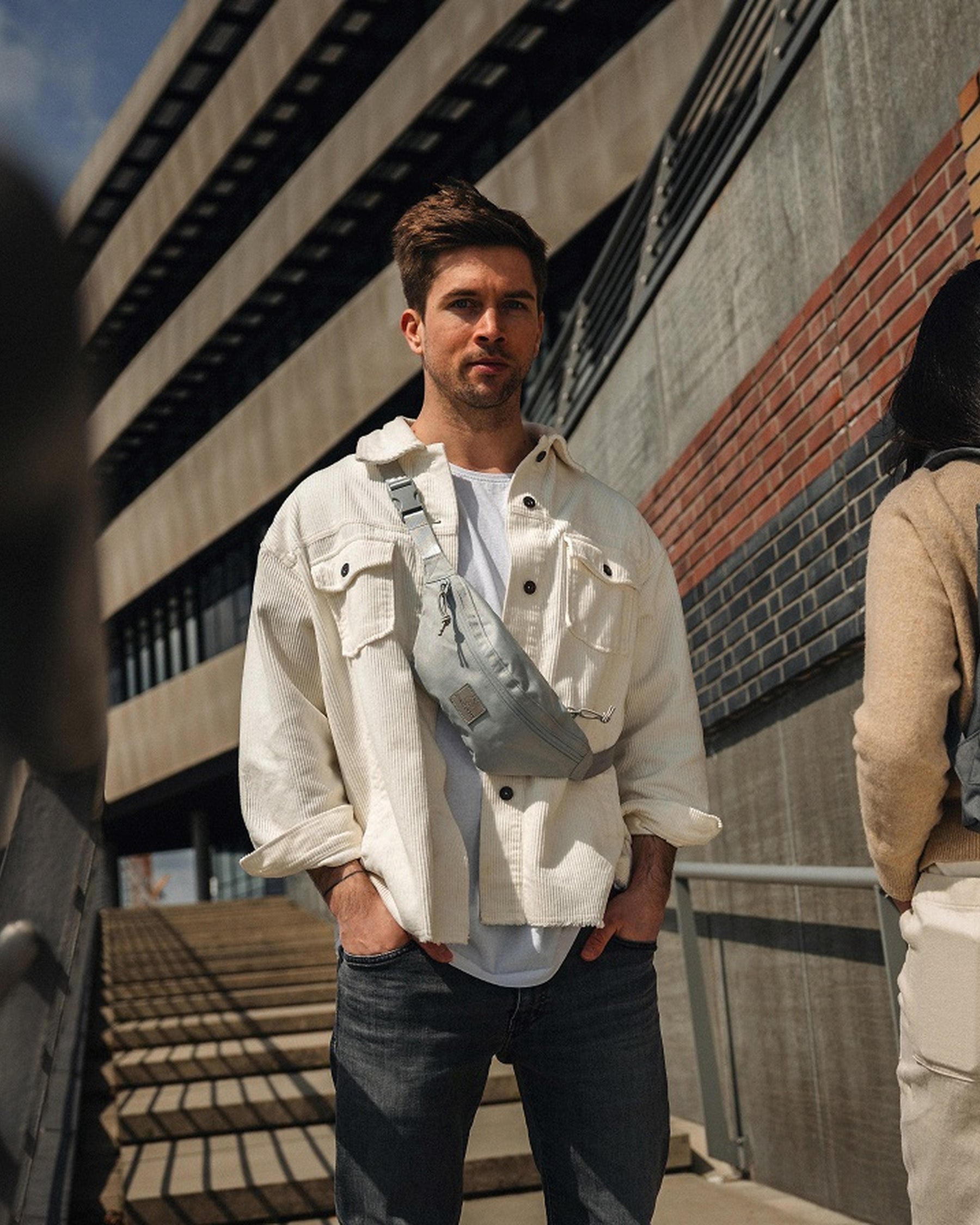 Mann trägt graue Bauchtasche 'Erik Small' quer am Oberkörper, weiße Jacke, weiße T-Shirt, schwarze Jeans
