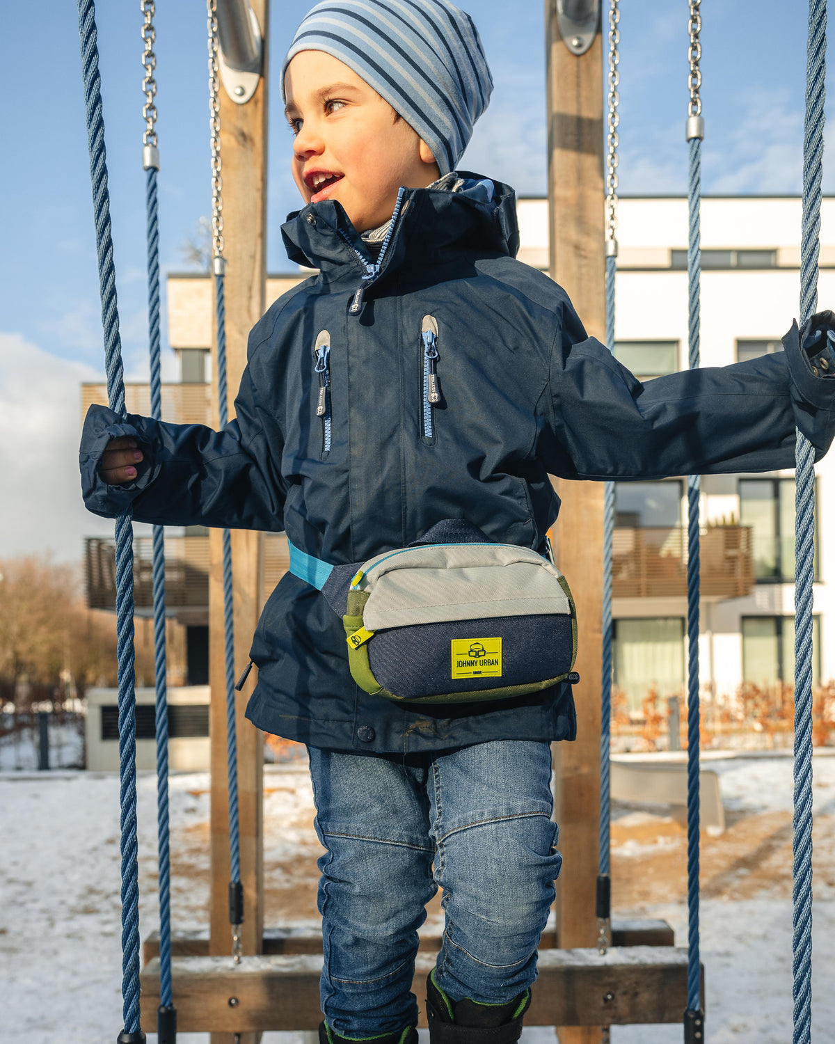 Kind trägt Kinder Bauchtasche 'Felix' in Blau, Weiß und Grün beim Balancieren auf einem Seil im Schnee
