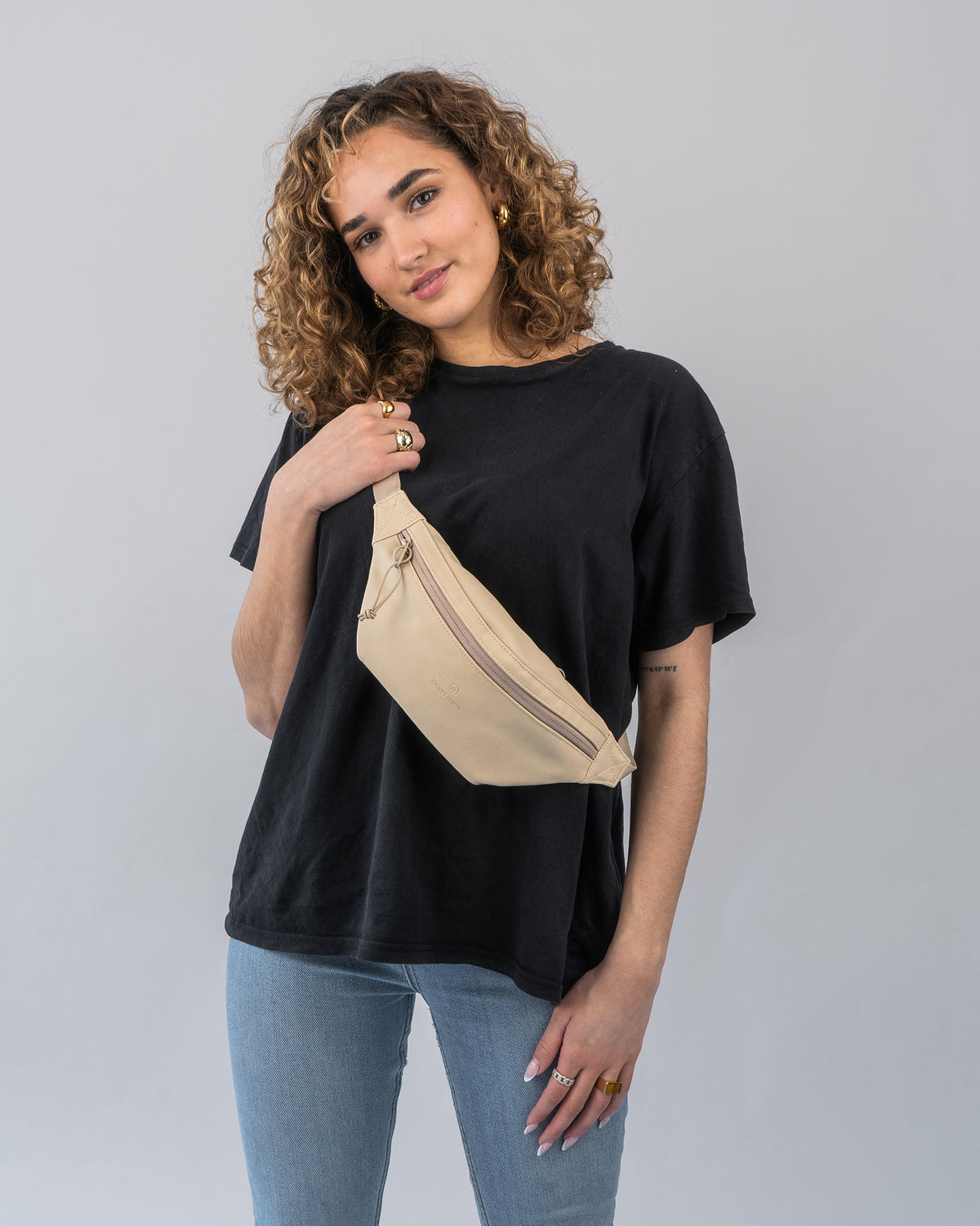 Frau trägt beige Bauchtasche 'Toni' aus Kunstleder über der Schulter zu schwarzem T-Shirt und blauen Jeans