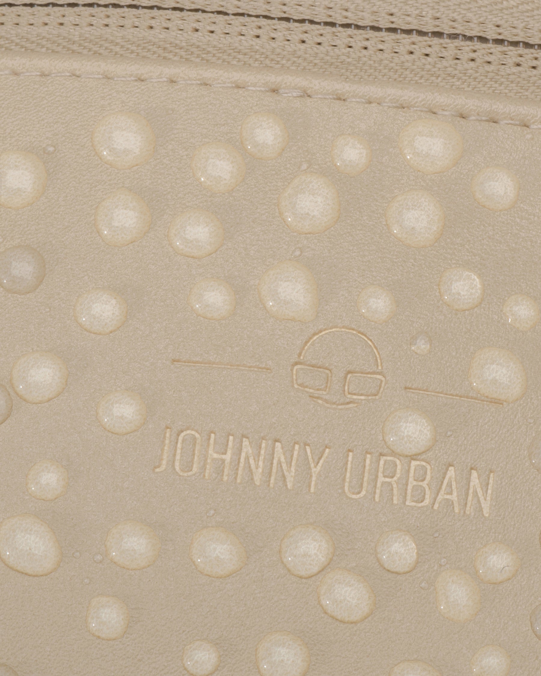 Nahaufnahme der wasserabweisenden, beigefarbenen Kunstleder-Oberfläche der Bauchtasche 'Toni' mit Johnny Urban Logo