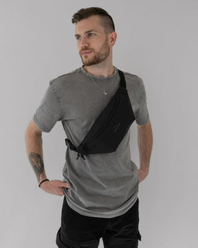 Mann mit grauem T-Shirt trägt die schwarze Bauchtasche 'Riley' von Johnny Urban diagonal über der Brust