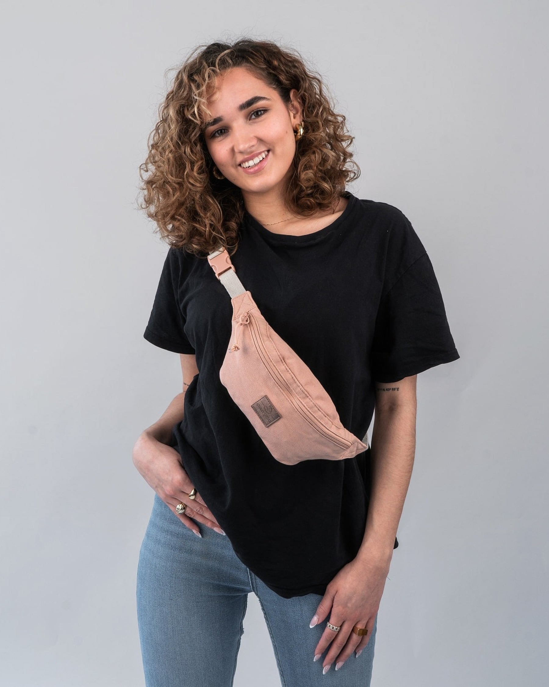 Frau trägt rosa Bauchtasche 'Toni' von Johnny Urban über schwarzem T-Shirt und blauen Jeans