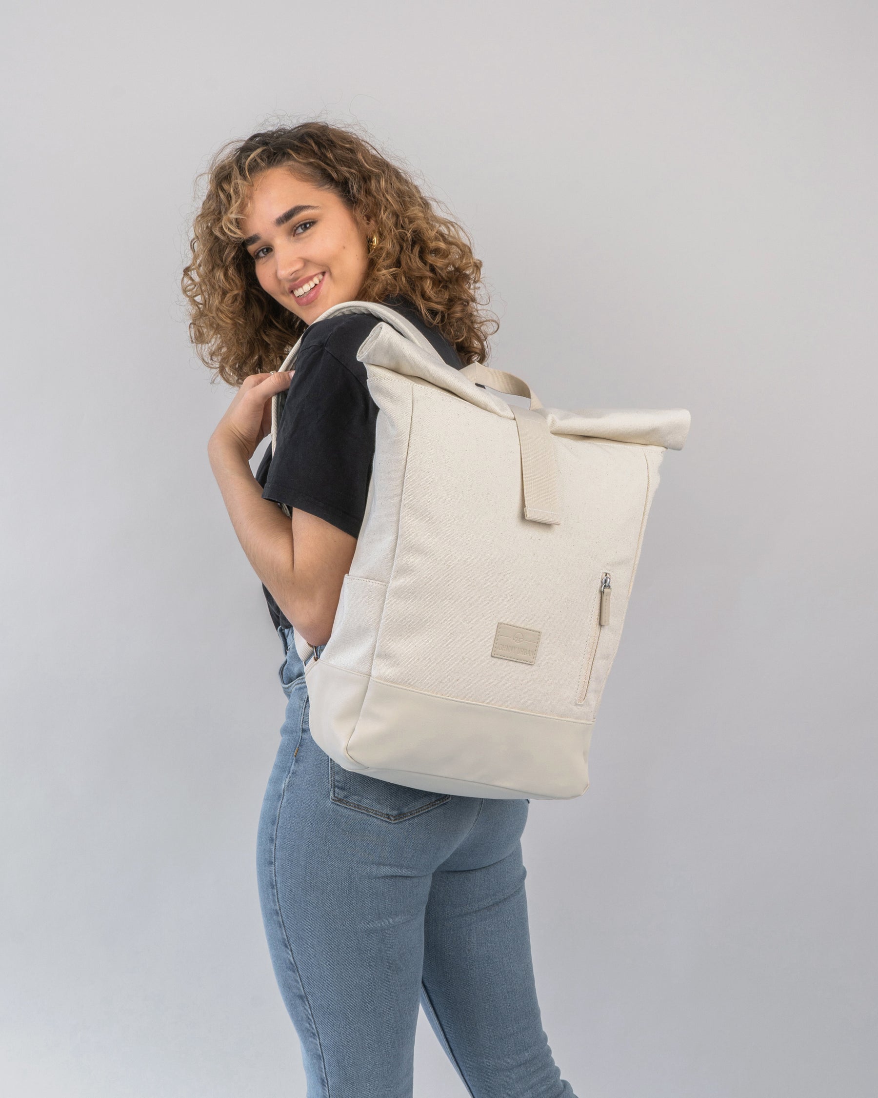 Frau trägt hellbeigen Rolltop Rucksack 'Adam Medium' aus Canvas mit Reißverschlussfach hinten