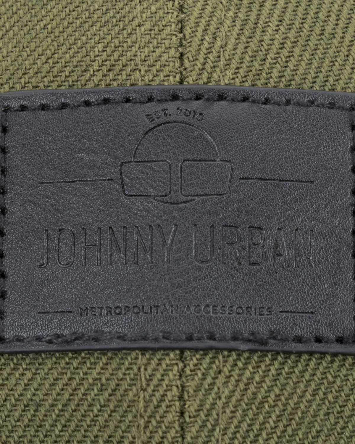 Schwarzes Lederetikett mit Johnny Urban Logo und Text auf grün-schwarzem Canvas-Material.