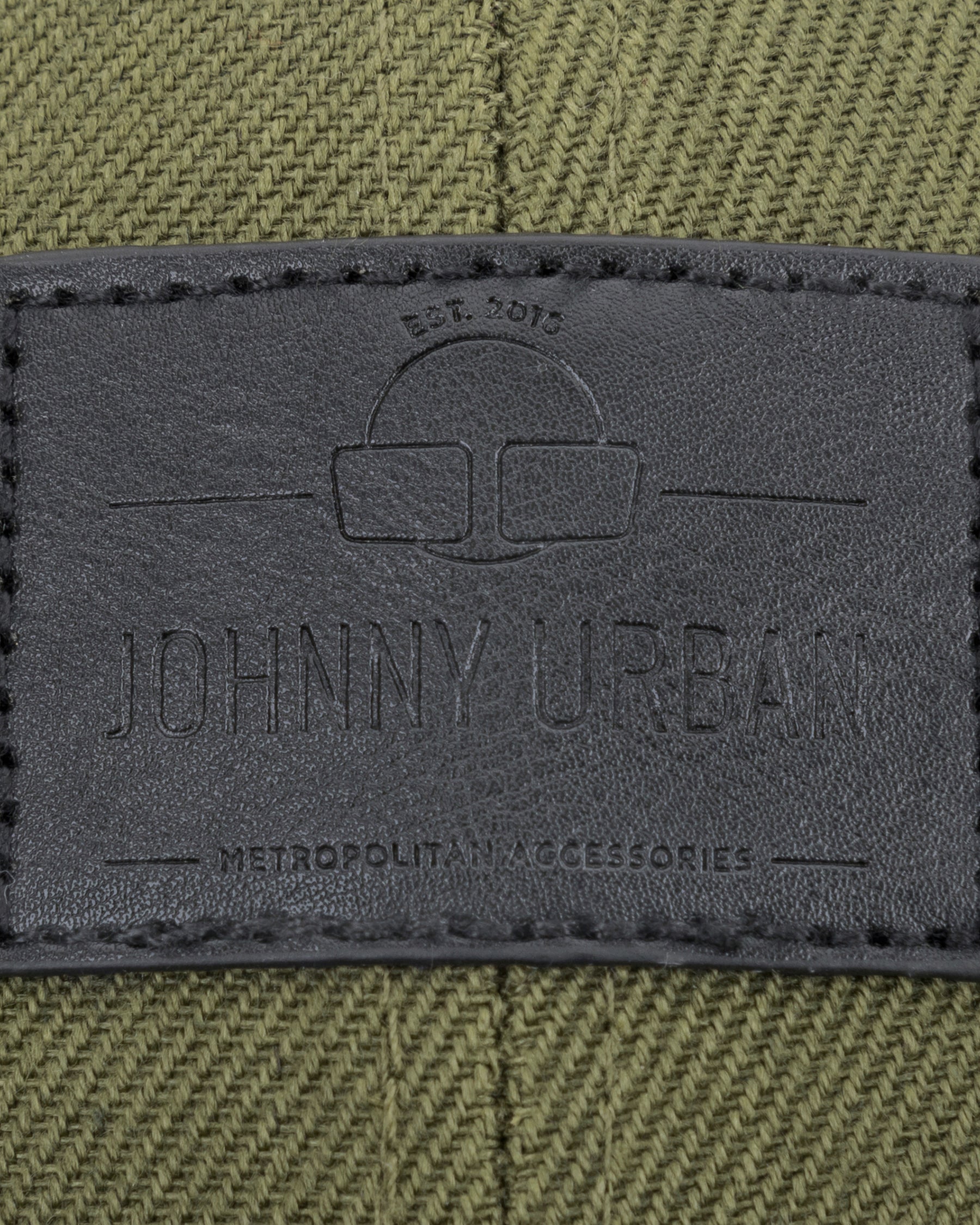 Schwarzes Lederetikett mit Johnny Urban Logo und Text auf grün-schwarzem Canvas-Material.